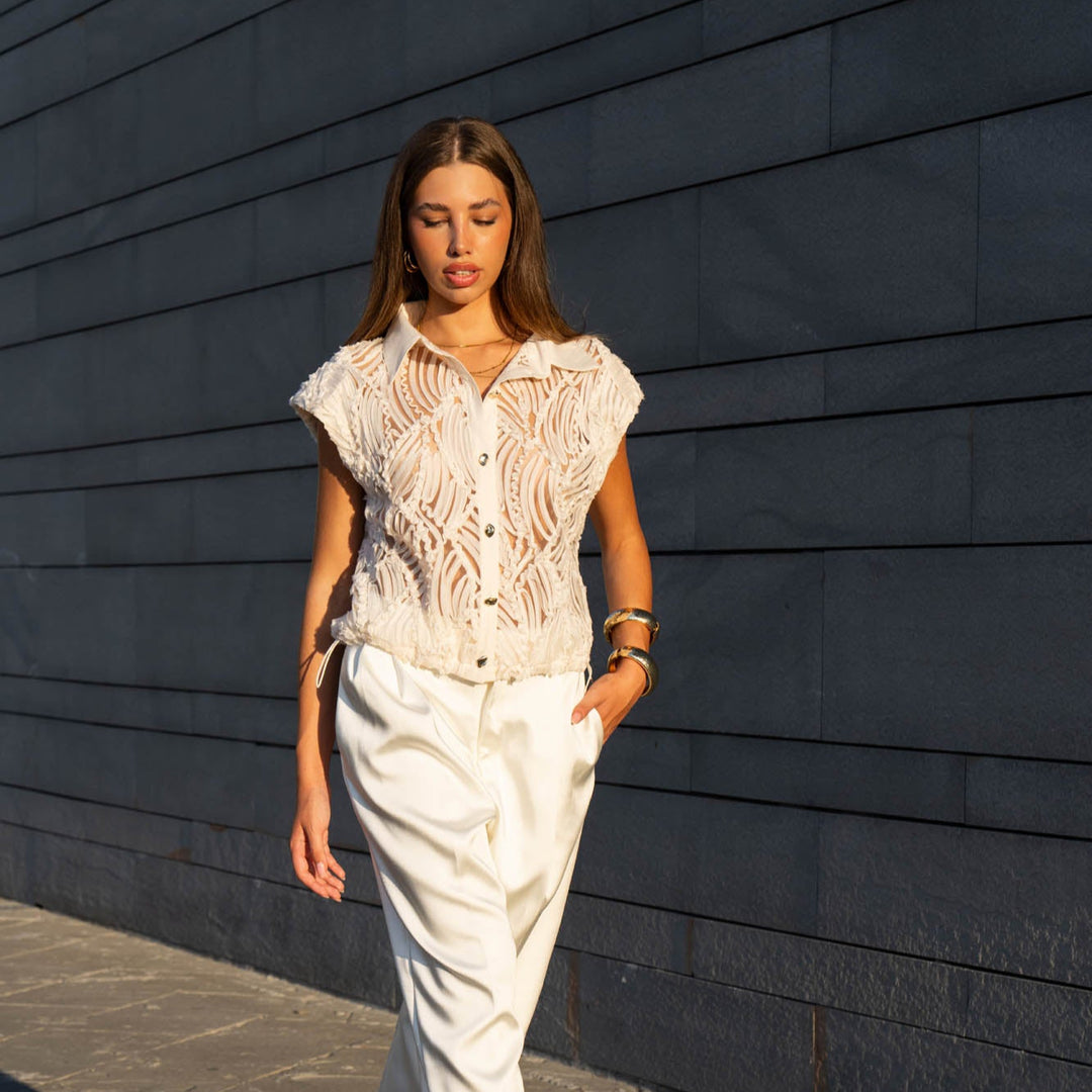 Woman in a white outfit standing against a dark wall.